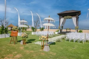 An outdoor beach wedding setup with rows of chairs and decorative umbrellas arranged on a grassy area.