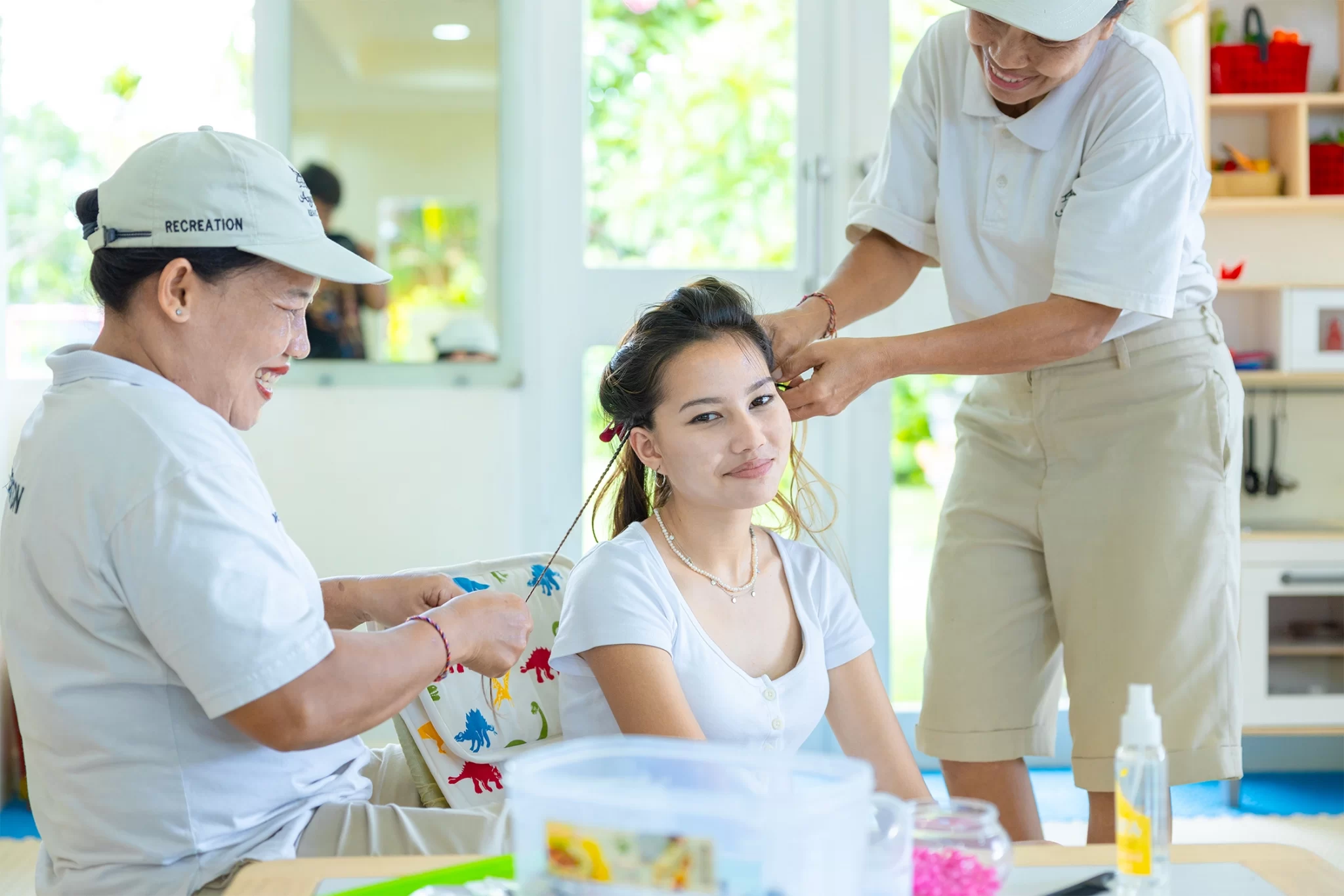 a girl is enjoying her hair braided by 2 women at a camp ananda kid ayodya