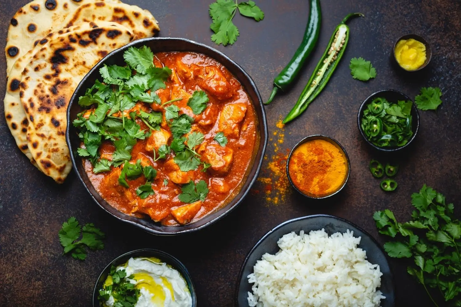 A plate of Chicken Tikka Masala with rice and pita bread, set against a dark background.