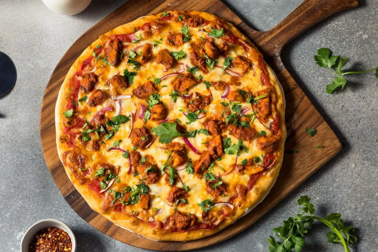 Chicken Tikka Pizza featuring melted cheese and herbs, artfully arranged on a wooden serving board.