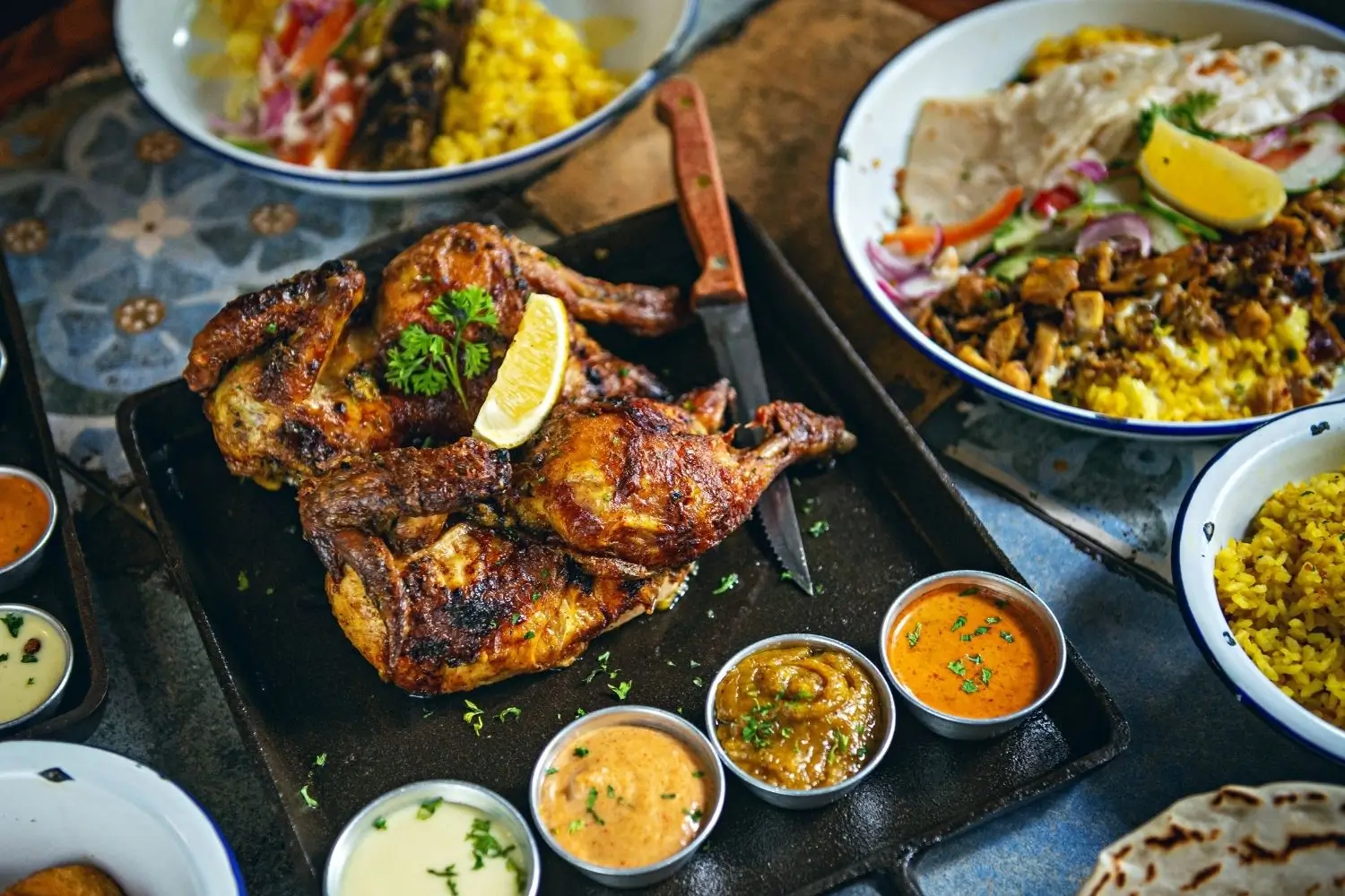 A diverse spread of dishes on a table, highlighted by Tandoori Chicken as a key item.
