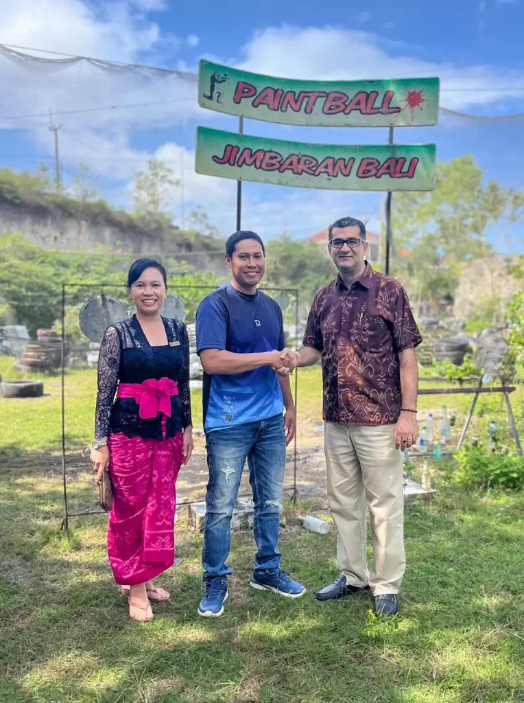 Two individuals shaking hands in front of a sign, symbolizing agreement paintball bali arena