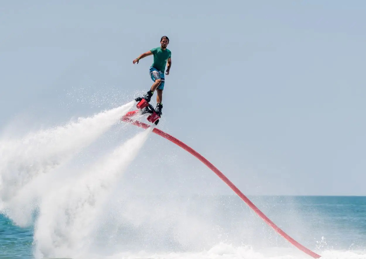  A man riding a flyboarding on the water on a sunny day.