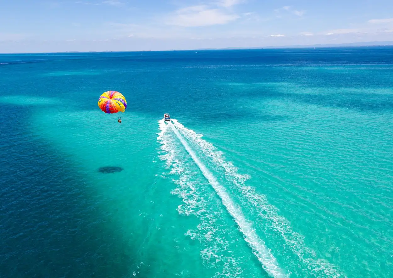 A person parasailing above the ocean, with a colorful parachute soaring against a clear blue sky.
