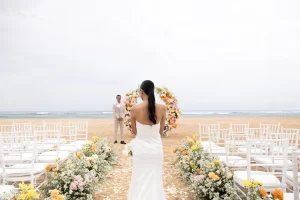 A bride walking down the aisle at a beach wedding in Nusa Dua, Bali, with the ocean in the background.
